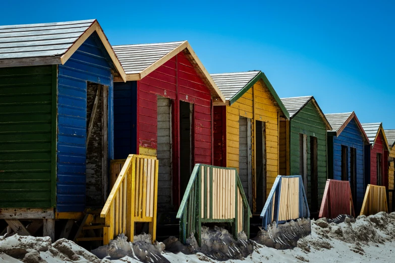 many different colored wooden beach huts lined up against the sand