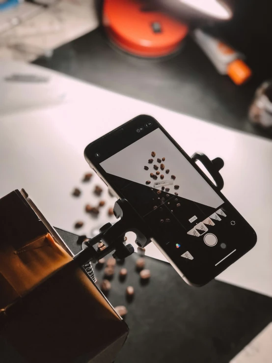 a coffee cup being filled with beans with a smartphone and the coffee maker in the background