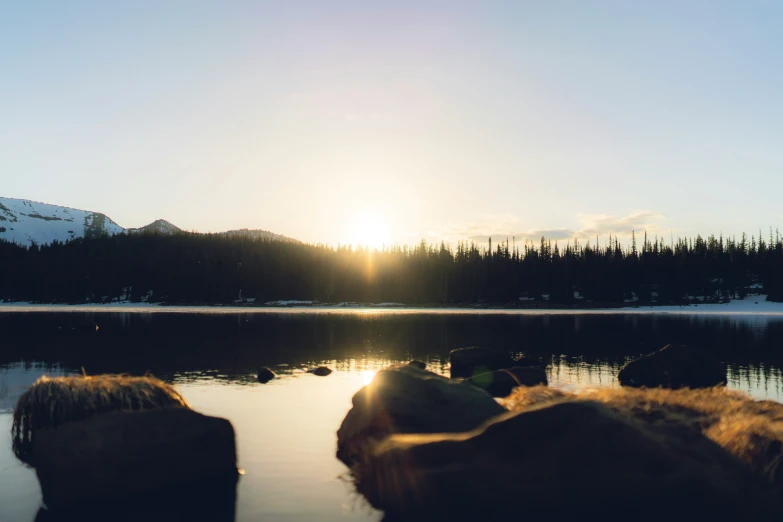 a landscape image with the sun setting over some snow capped hills