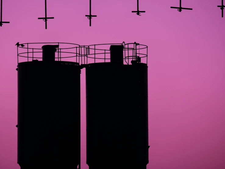 black silos in silhouette against a pink sky