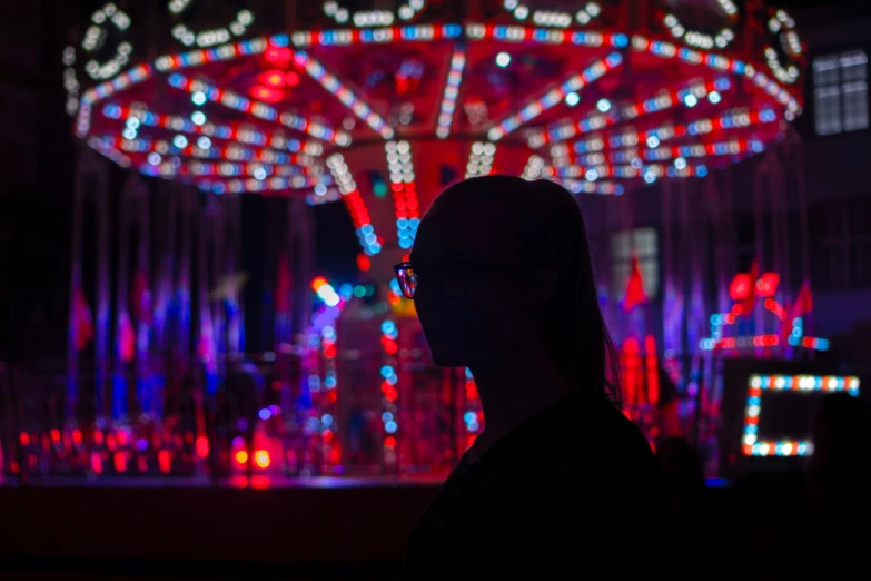 the silhouette of a man's face as he looks down at a lit up carousel