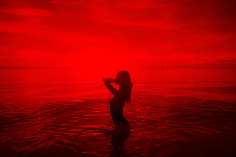 a woman is standing in the middle of the water, with red skies