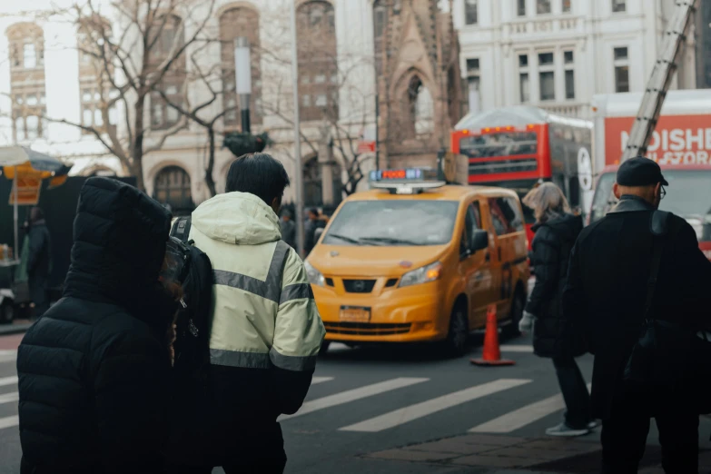 many people are walking down the street with a taxi cab in the back ground