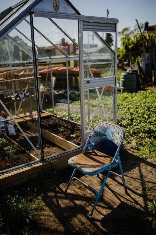 an old garden greenhouse with blue chair sitting in the grass