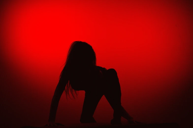 the silhouette of a woman sitting alone against a red background