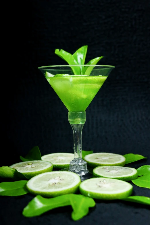 a green drink on a black table with lime slices