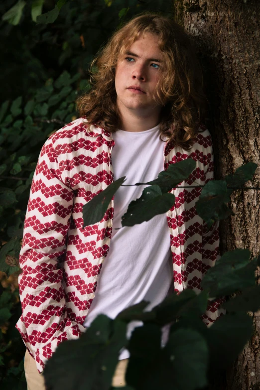 the man is leaning against the tree wearing a sweater