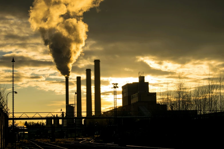 the sun is setting on a smokestack behind several pipes