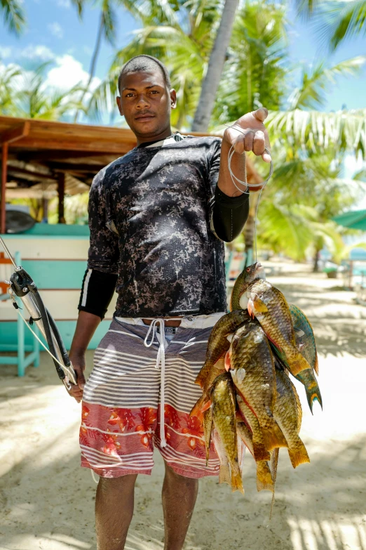 man wearing shorts standing on a beach holding two fish