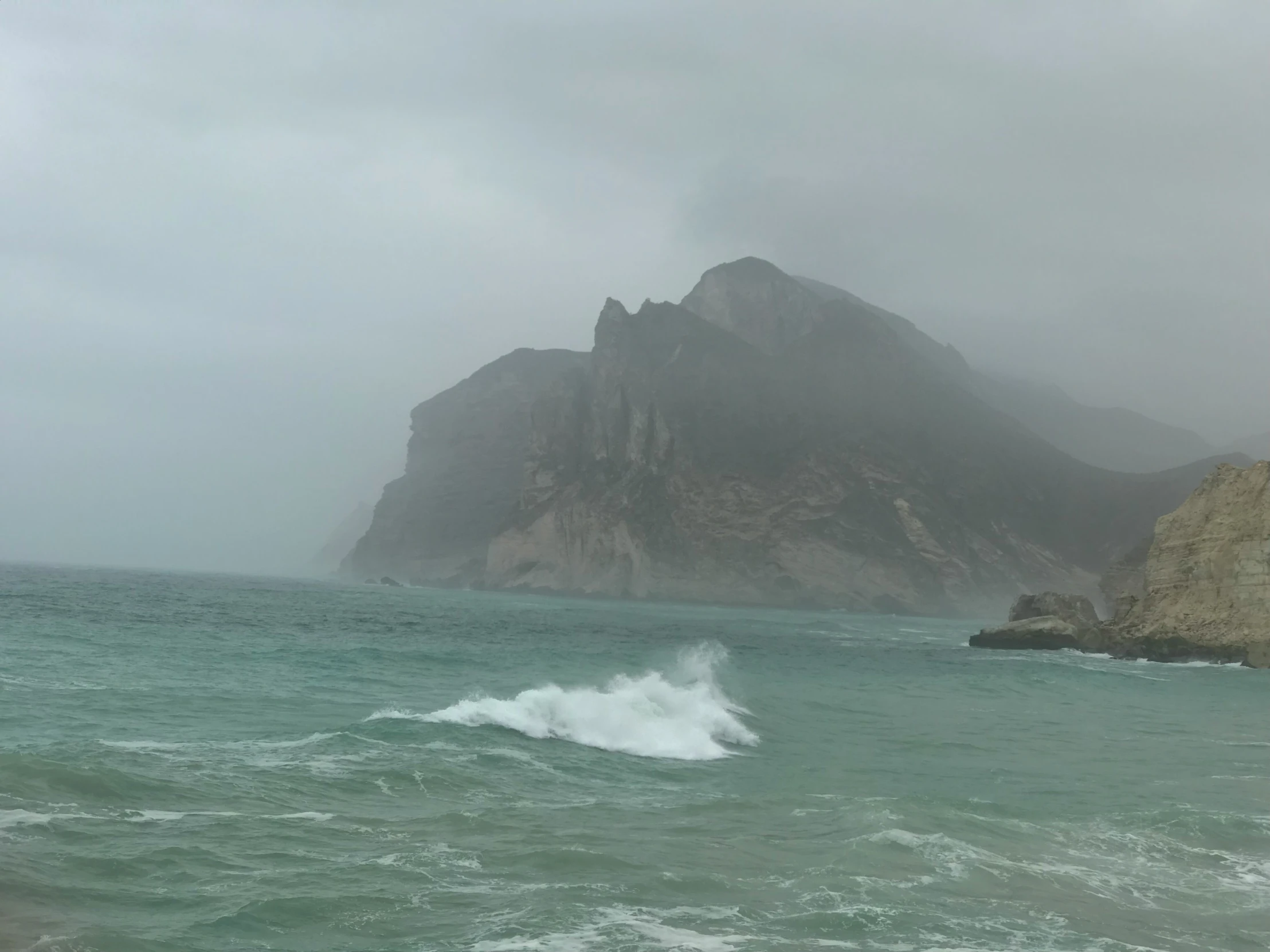 a wave splashes in the ocean on an overcast day