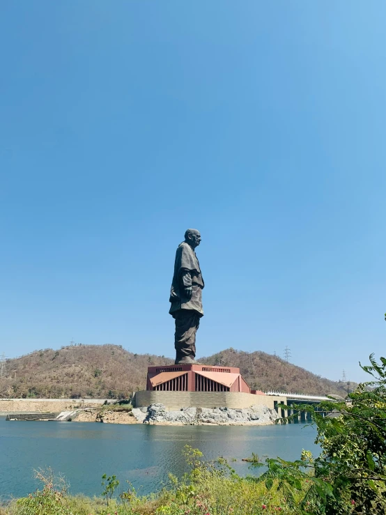 an iron statue sitting on top of a hill next to water
