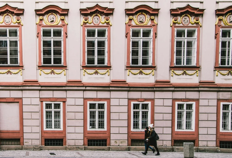 people walking down a sidewalk near tall pink buildings