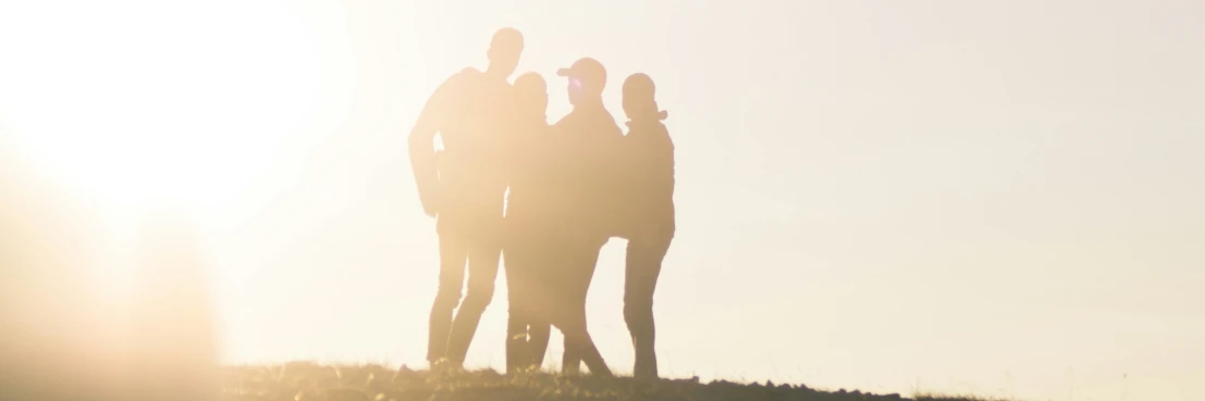 four people standing on a hill in front of the sun