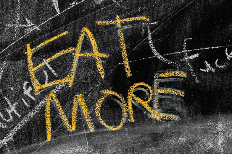 a chalk drawing saying eat more is written in bright yellow markeres