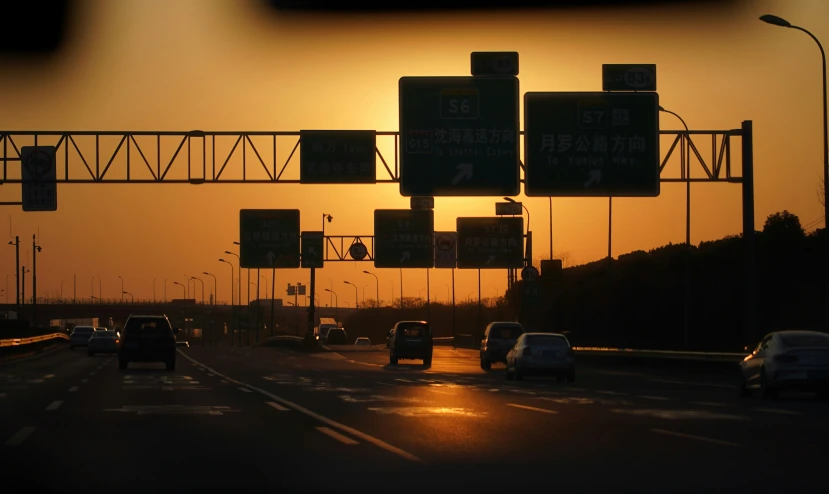 some street signs and cars on a highway at sunset