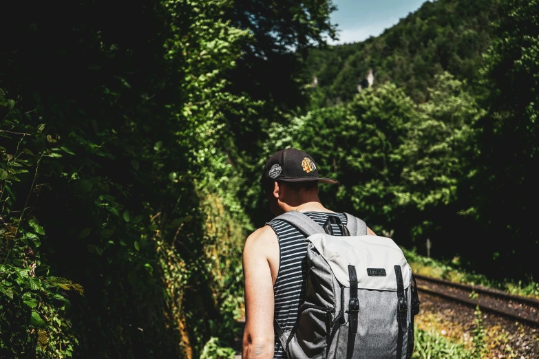 man on train tracks wearing backpack and hat