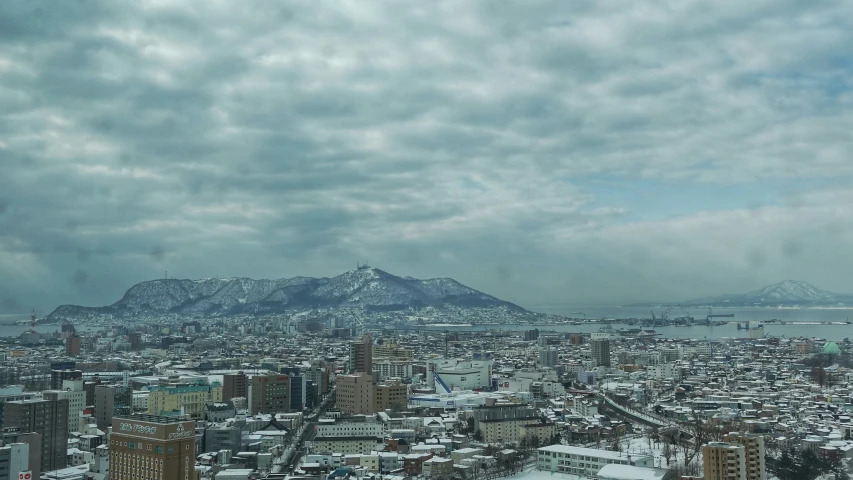 a cloudy view of a city with a snow covered mountain in the distance