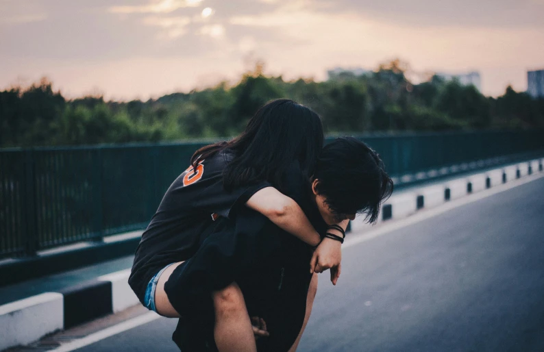 man carrying woman across street with bridge in background