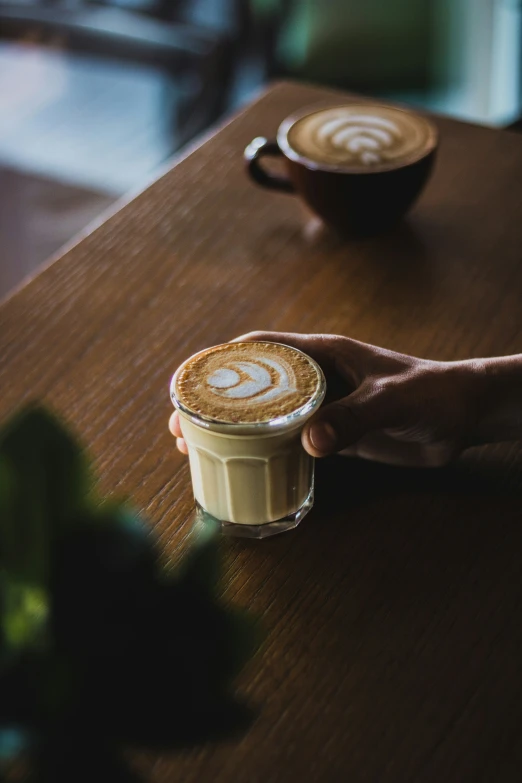 someone holds the lid of a coffee cup as another cup sits on the table