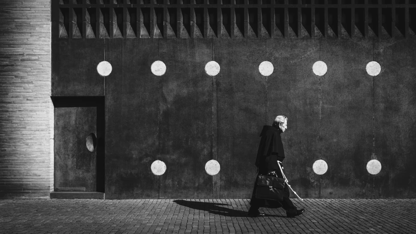 a man walks across a sidewalk next to a wall covered in round holes