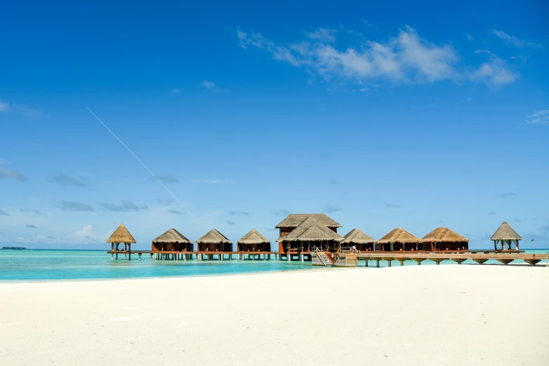 a sandy beach with thatched roof huts on the water