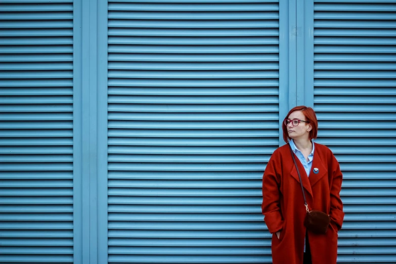 a woman standing next to a blue wall wearing a long red coat