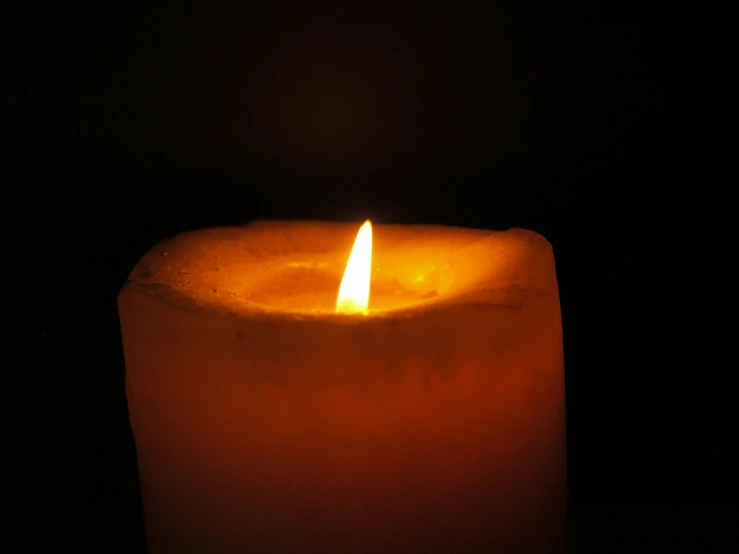 a lit candle in the dark with no visible lights