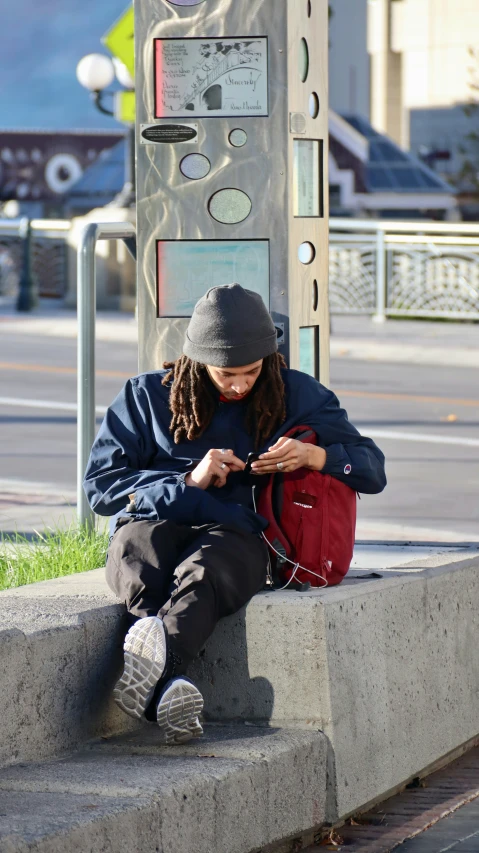 person sitting on steps next to a street with a red bag on his lap