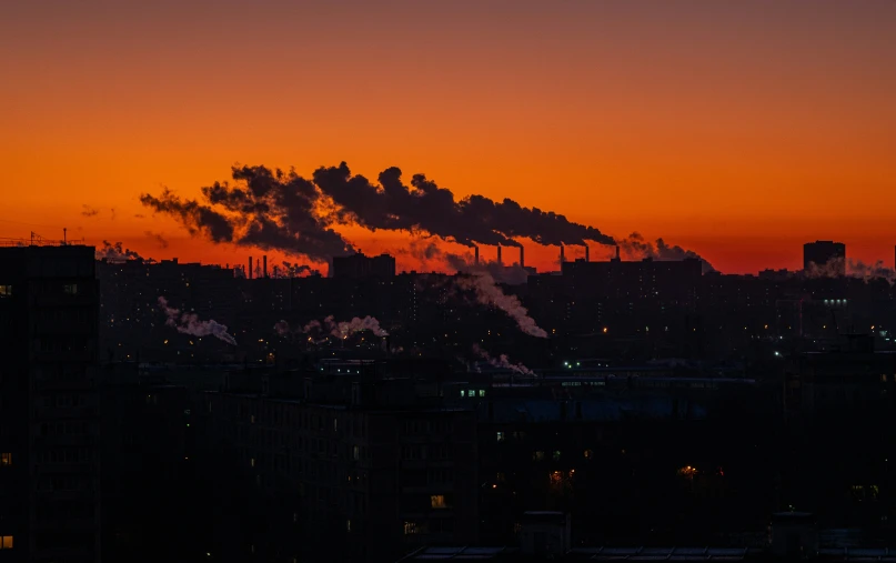 a factory with smoke pouring out of it at sunset