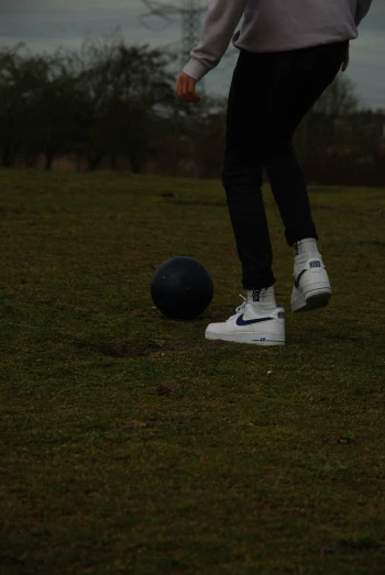 a person in sneakers and a nike cleated stands by a ball on the grass