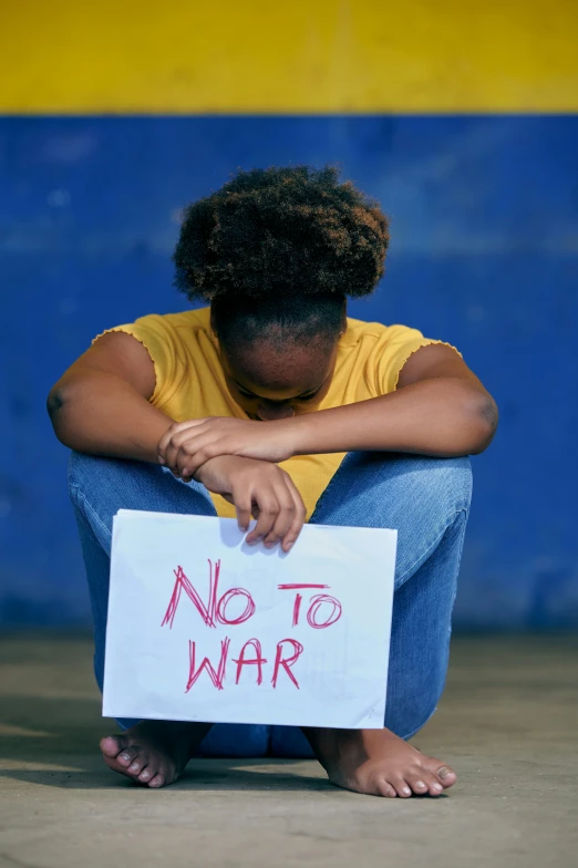 a woman squatting on the ground with a sign saying no to war