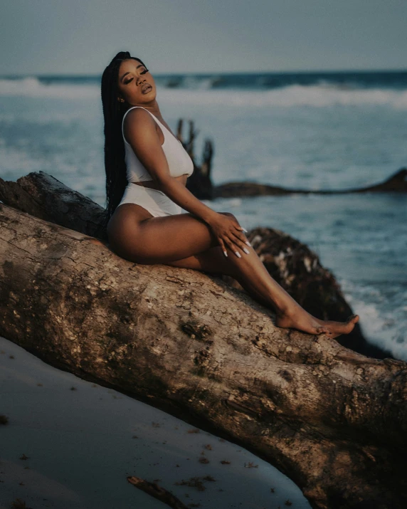 a woman with long hair sitting on a log near the water