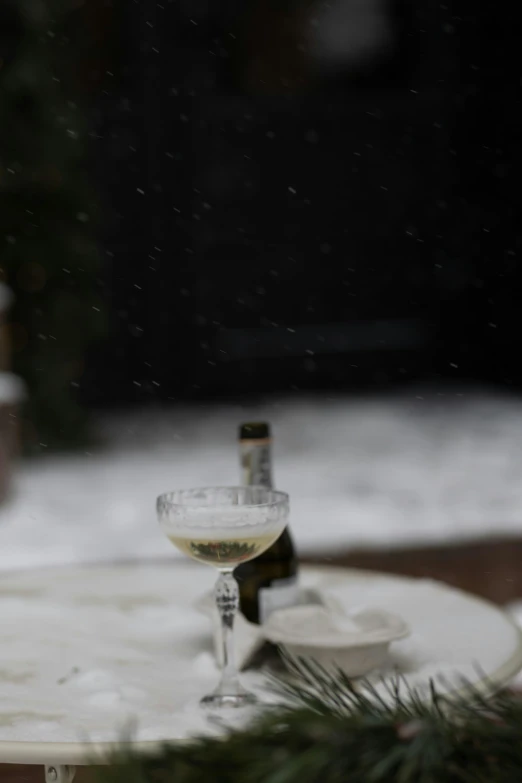 two glasses with a couple of bottles of wine are sitting on the side of a table covered in snow