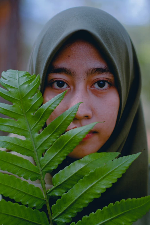 the  is hiding her face behind a green leaf