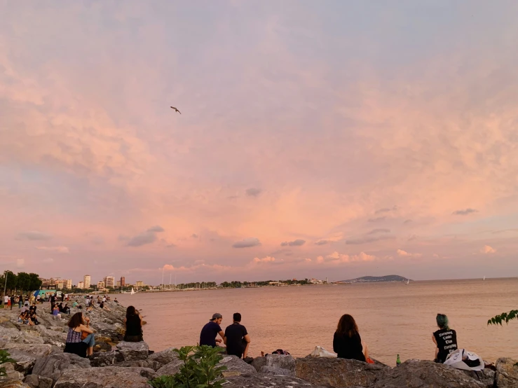 a group of people are sitting on rocks and staring out at the water