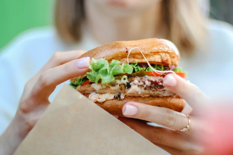 a young lady eating a sandwich next to a cardboard bag