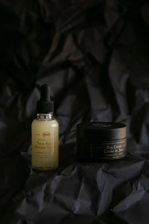 a bottle of cream and a jar of skin care products on a gray cloth