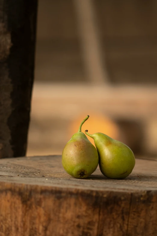 two small green pears are sitting on a wooden stool