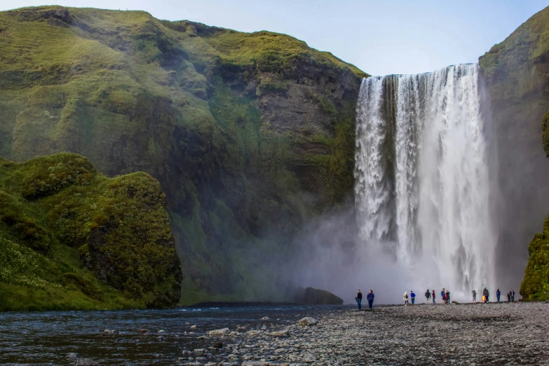 a large waterfall falling into the water with a group of people standing around it