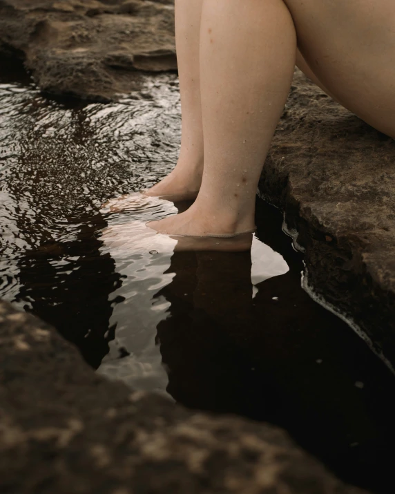 a person with bare feet standing in water next to a rock