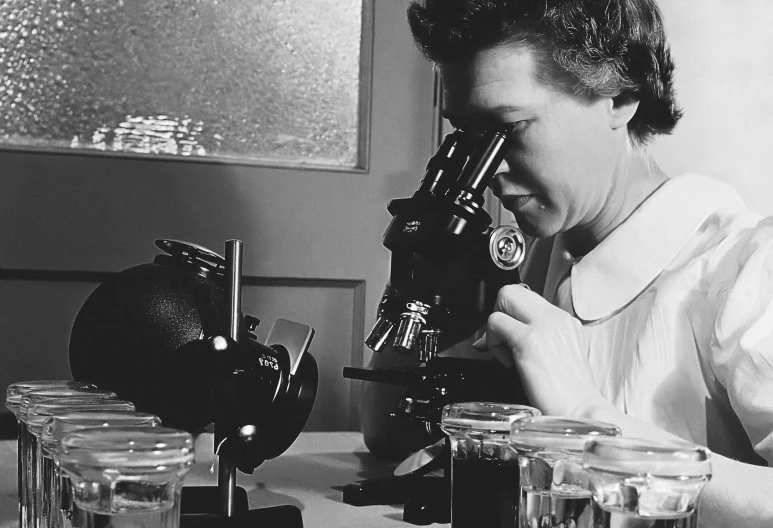 woman using a microscope in a lab filled with glass jars