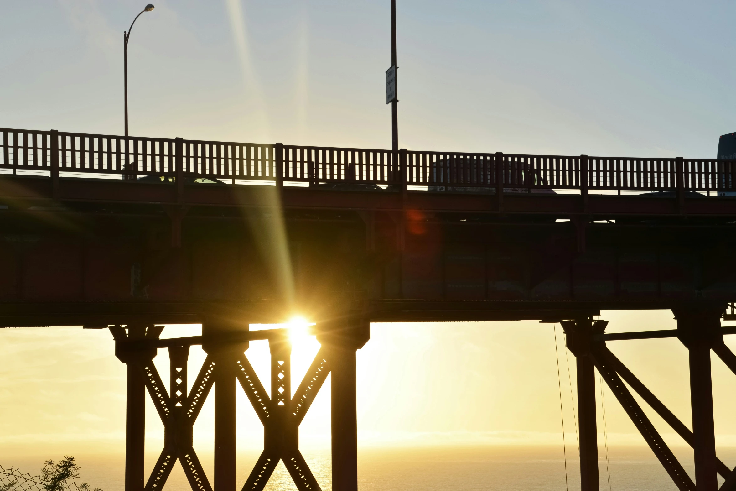 the sun sets behind a bridge across the ocean