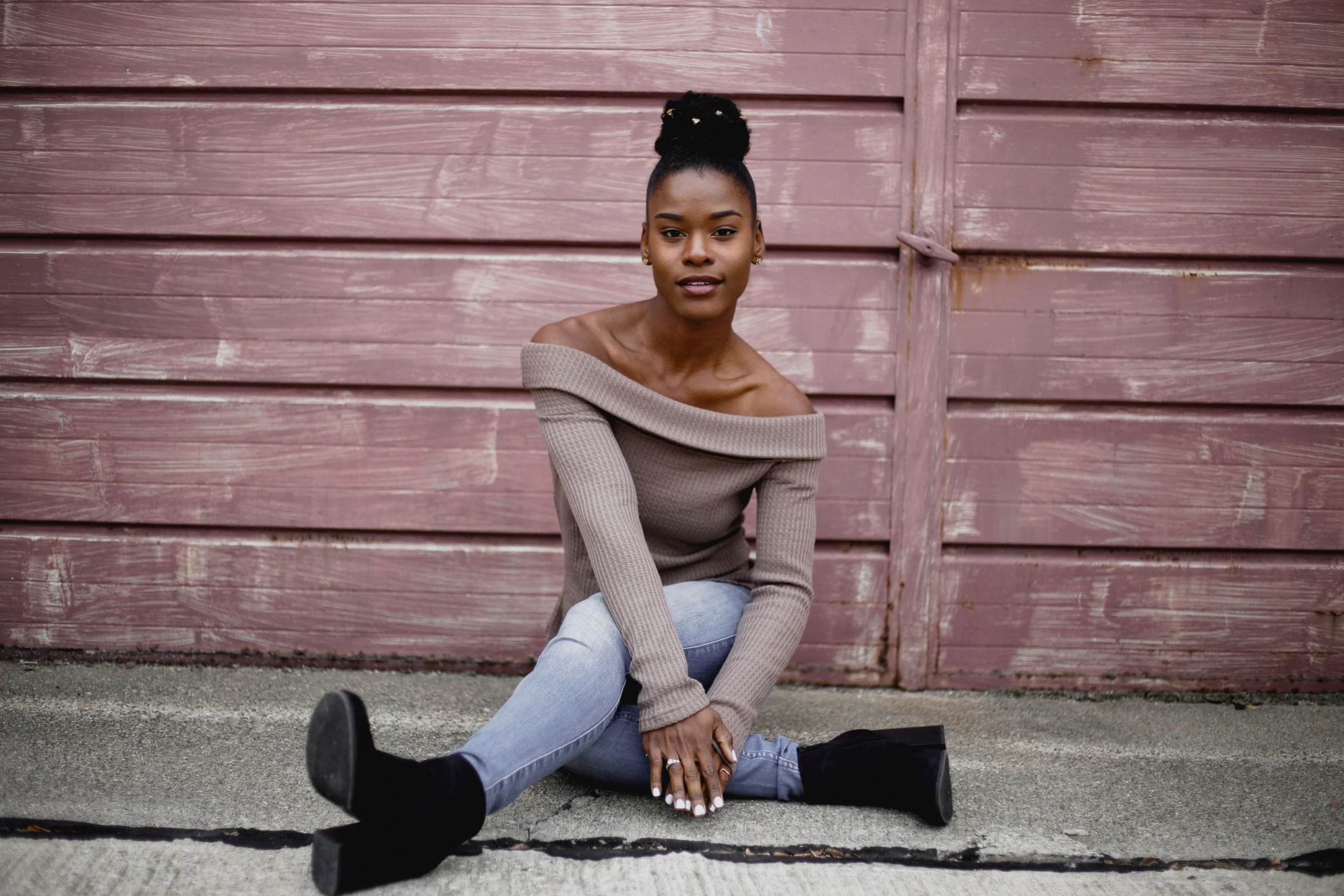 a black woman sitting on the ground in front of a pink wall