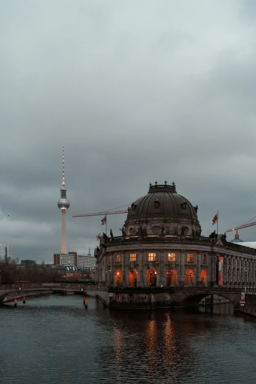 a building is on a dark water with cranes in the background