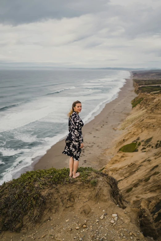 a woman in a dress looks over a cliff toward the ocean