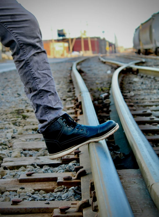 the shoe of a man is stepping on some train tracks