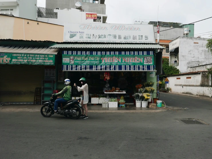 two people standing outside a store with a motorbike in front