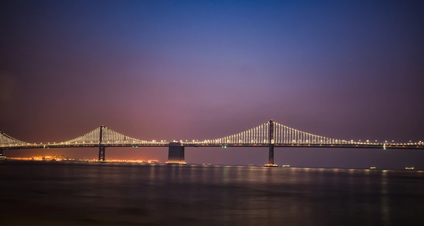 a long bridge crossing the water at night