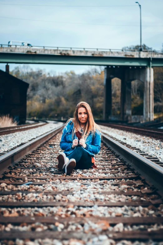 a beautiful young blond sitting on the tracks of train tracks