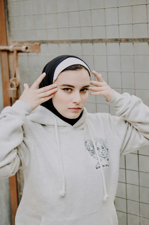 a girl in a white sweatshirt and black headband holding her hair up to the side